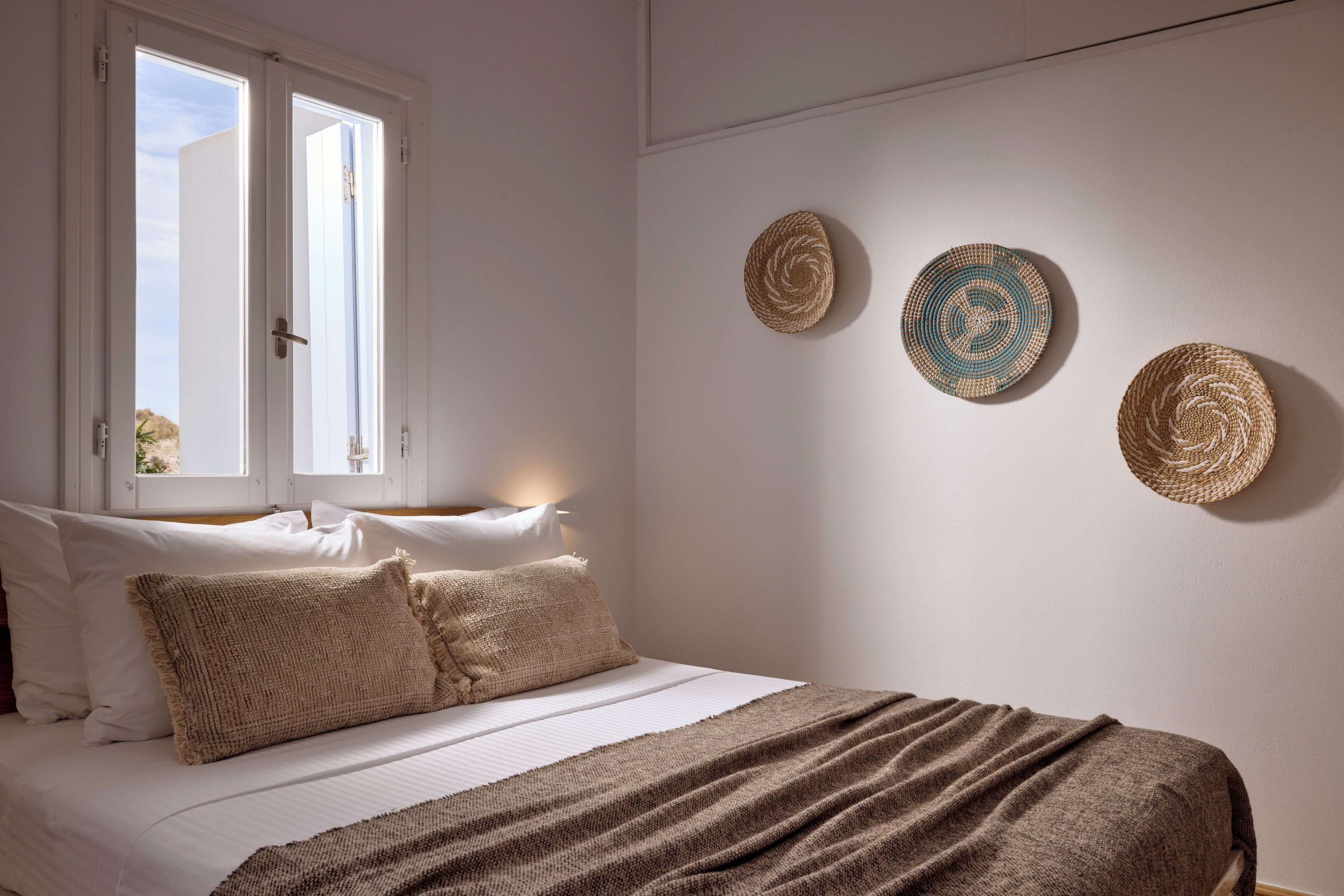 A bedroom with a bed, pillows, a blanket, and wall-mounted woven baskets.