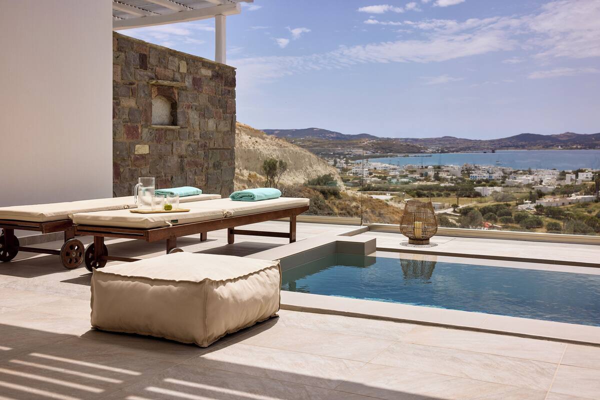 A poolside area with lounge chairs, a small pool, and a view of a coastal town.