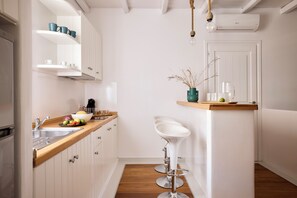 Una cocina con armarios blancos, encimera de madera, un fregadero y dos taburetes blancos.