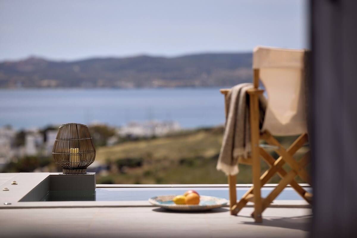 A view of a coastal landscape with a chair and a plate of fruit on a balcony.