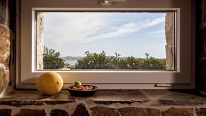 Une fenêtre donnant sur un mur de pierre, un panier de fruits et un citron posé sur le rebord.