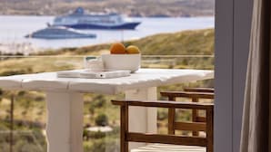 Une table avec un saladier rempli de fruits et un livre, donnant sur une étendue d’eau où l’on aperçoit un navire au loin.