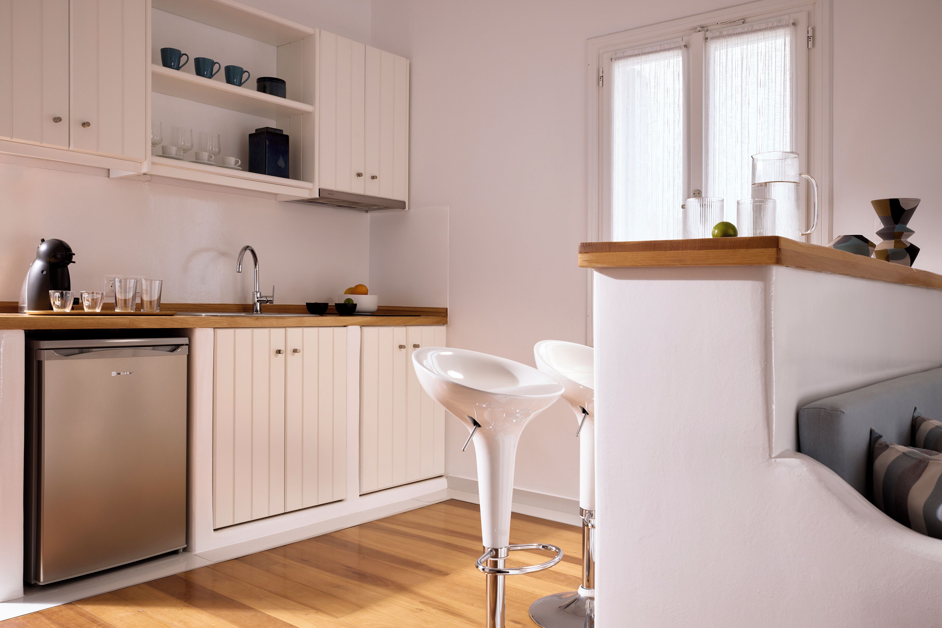 A modern kitchen with white cabinetry, a dishwasher, and two white bar stools.