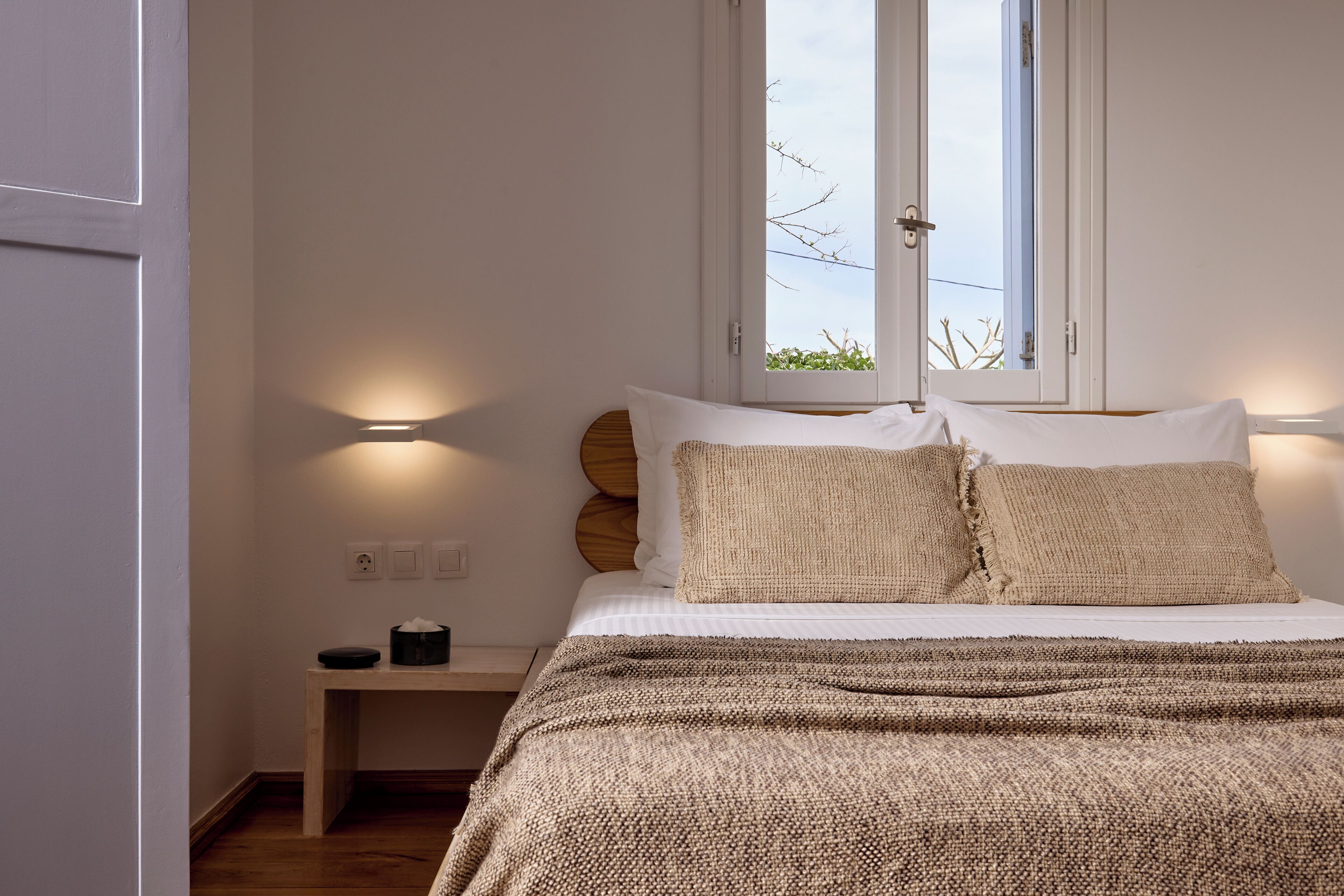 Un dormitorio con cama, mesita de noche, lámpara y ventana.
