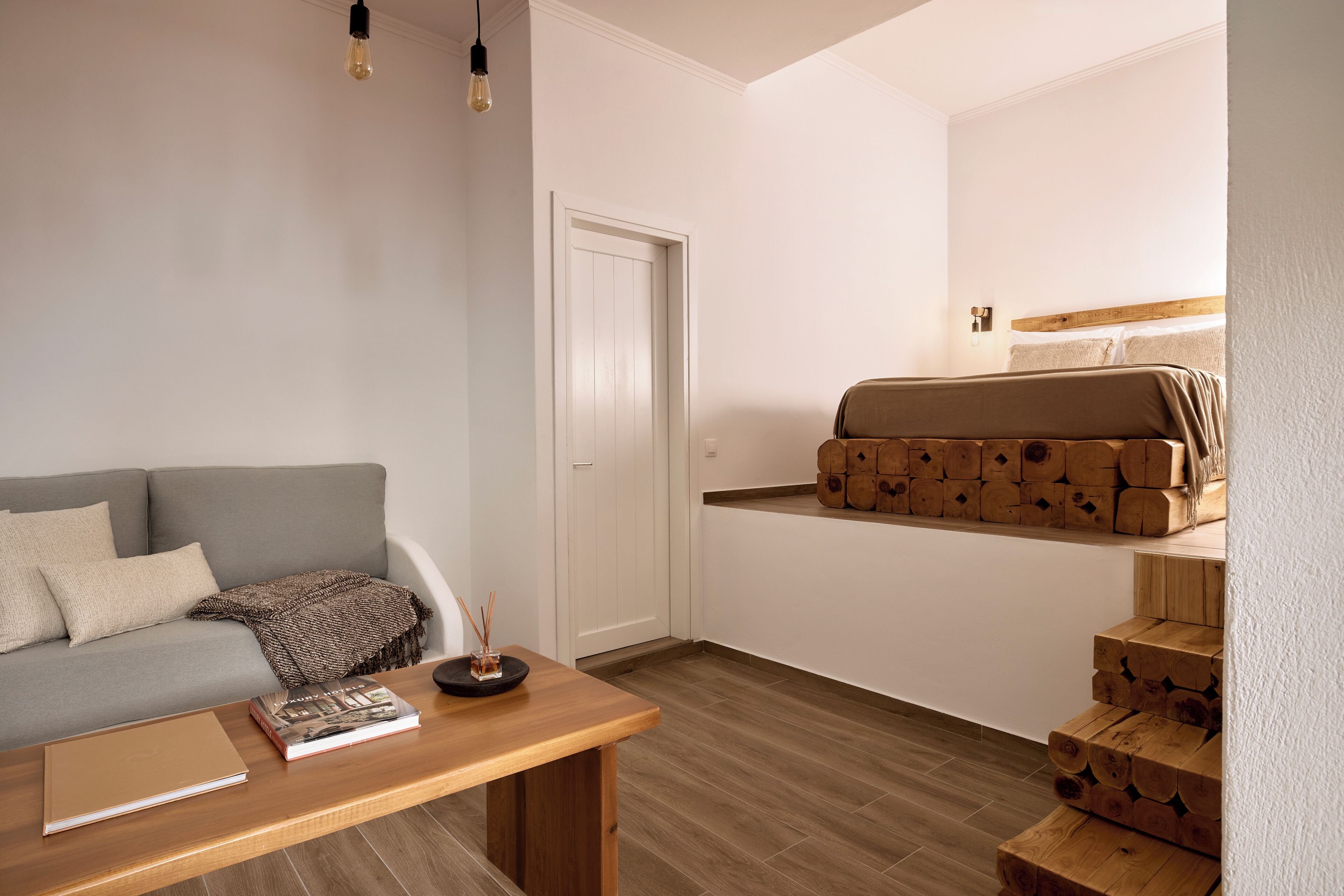 Un salon avec un canapé, une table basse sur laquelle se trouvent un livre et une bougie, et un escalier avec des marches en bois.