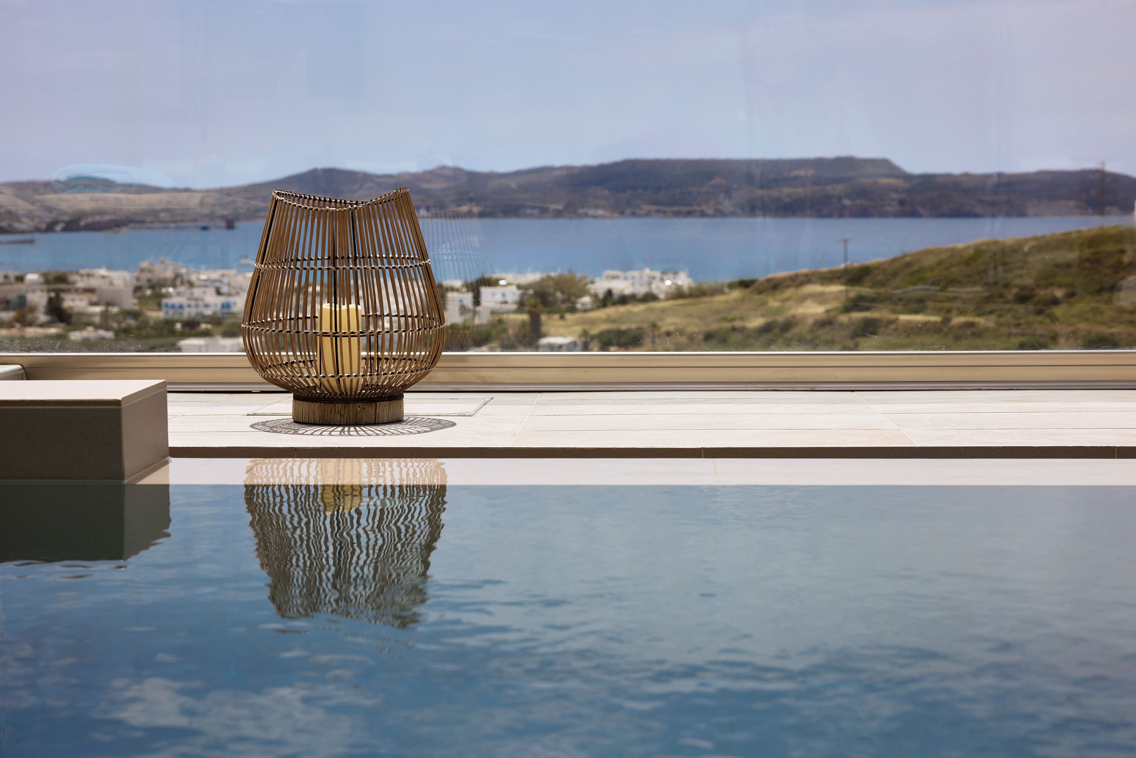 A modern pool area with a unique chair and a view of a lake and hills.