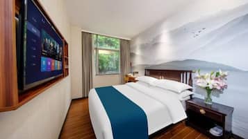A hotel room with a bed, a TV mounted on the wall, a nightstand, and a window with curtains.