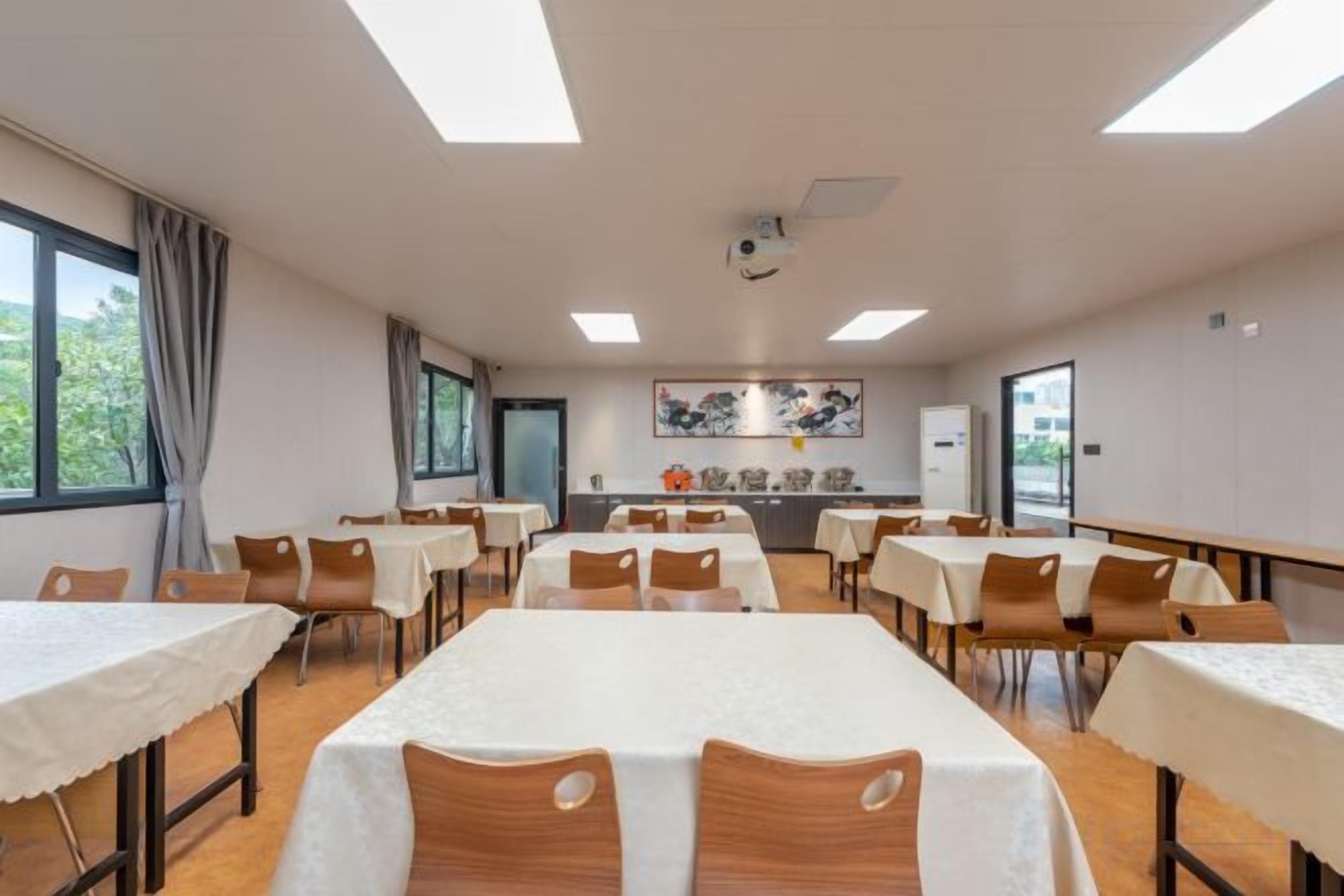 A conference room with tables and chairs, a projector, and a painting on the wall.