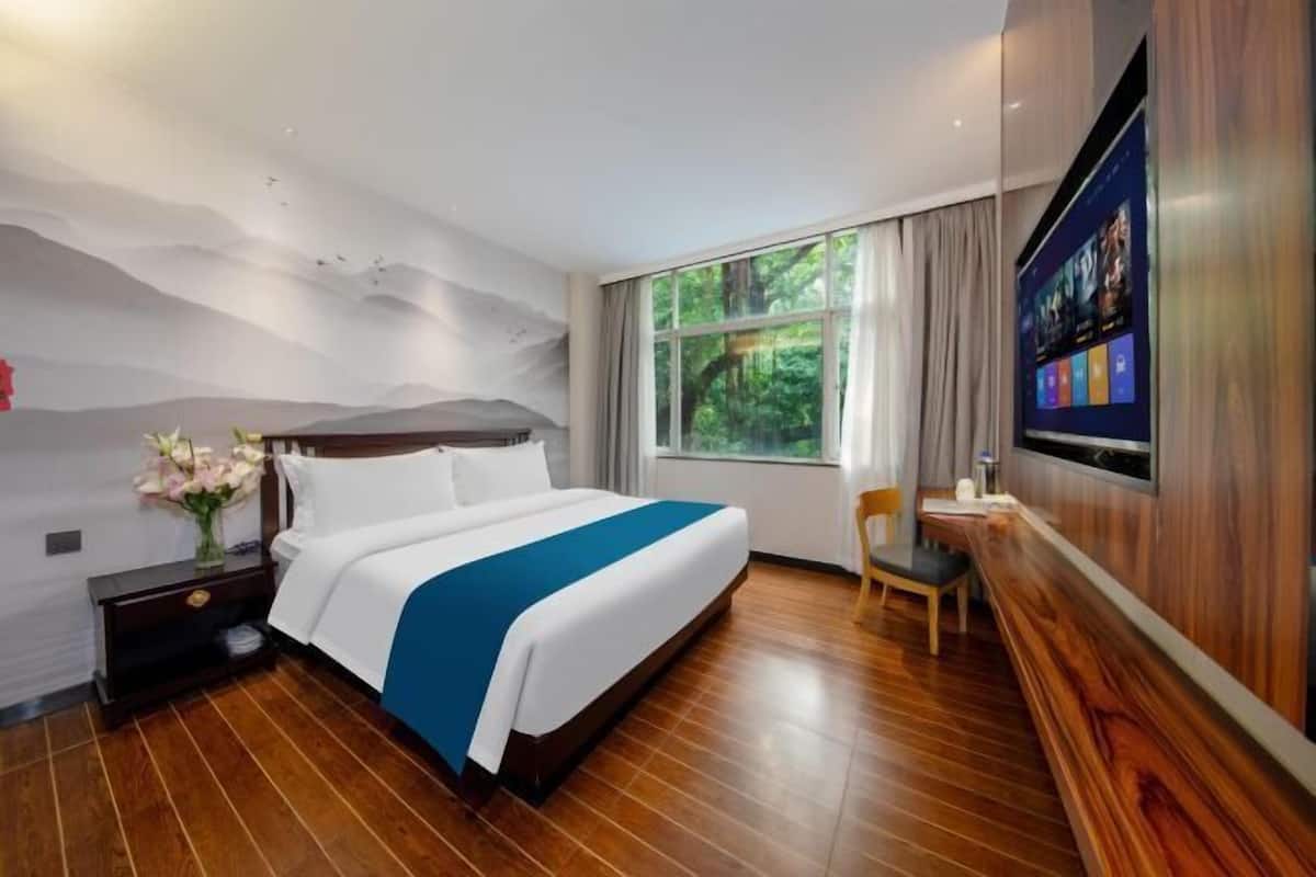 A hotel room with a bed, a desk, a TV, a window with curtains, and a wall with a nature mural.