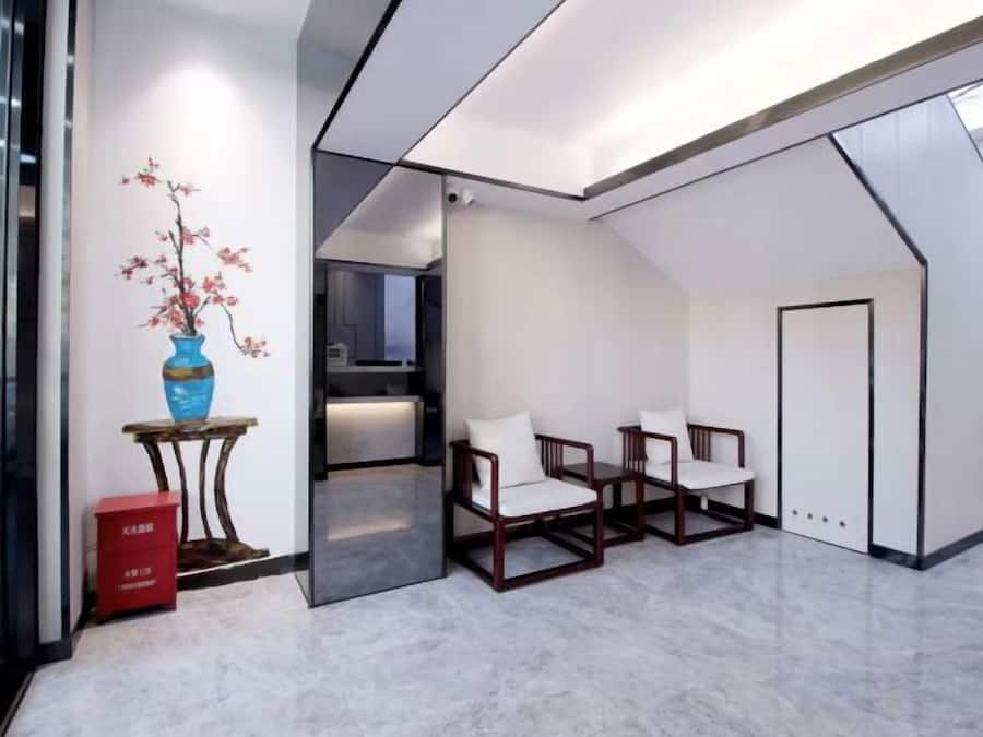 Un interior moderno con una zona de estar, un florero con flores y una cocina visible a través de una puerta abierta.