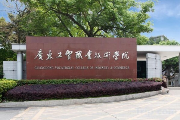 A sign for Guangdong Vocational College of Industry & Commerce with a modern building in the background. - Wenxing Hotel (Guangzhou Baiyun Mountain Plum Garden Metro Station) (Guangzhou)