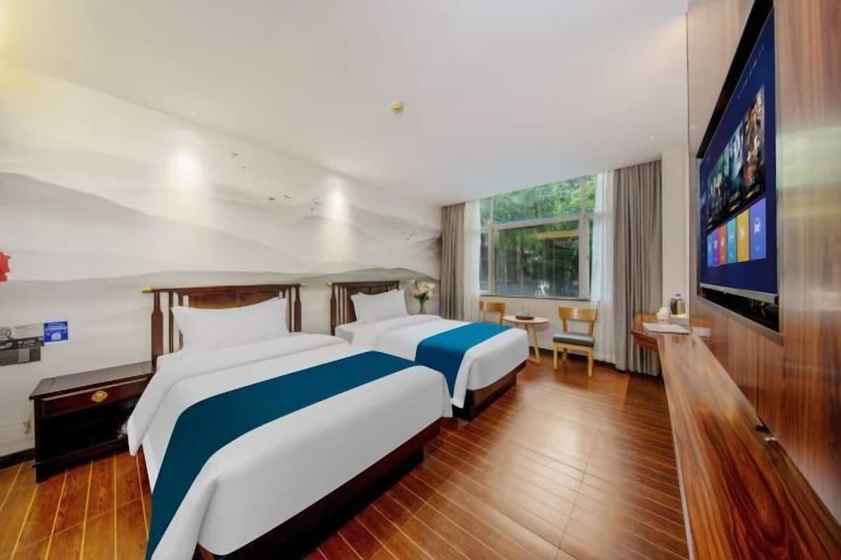 A hotel room with two beds, a TV, a small table, and a window with curtains.