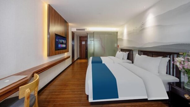 Ein modernes Hotelzimmer mit einem großen Bett, einem Schreibtisch, einem Fernseher und einer Glastür zum Badezimmer.