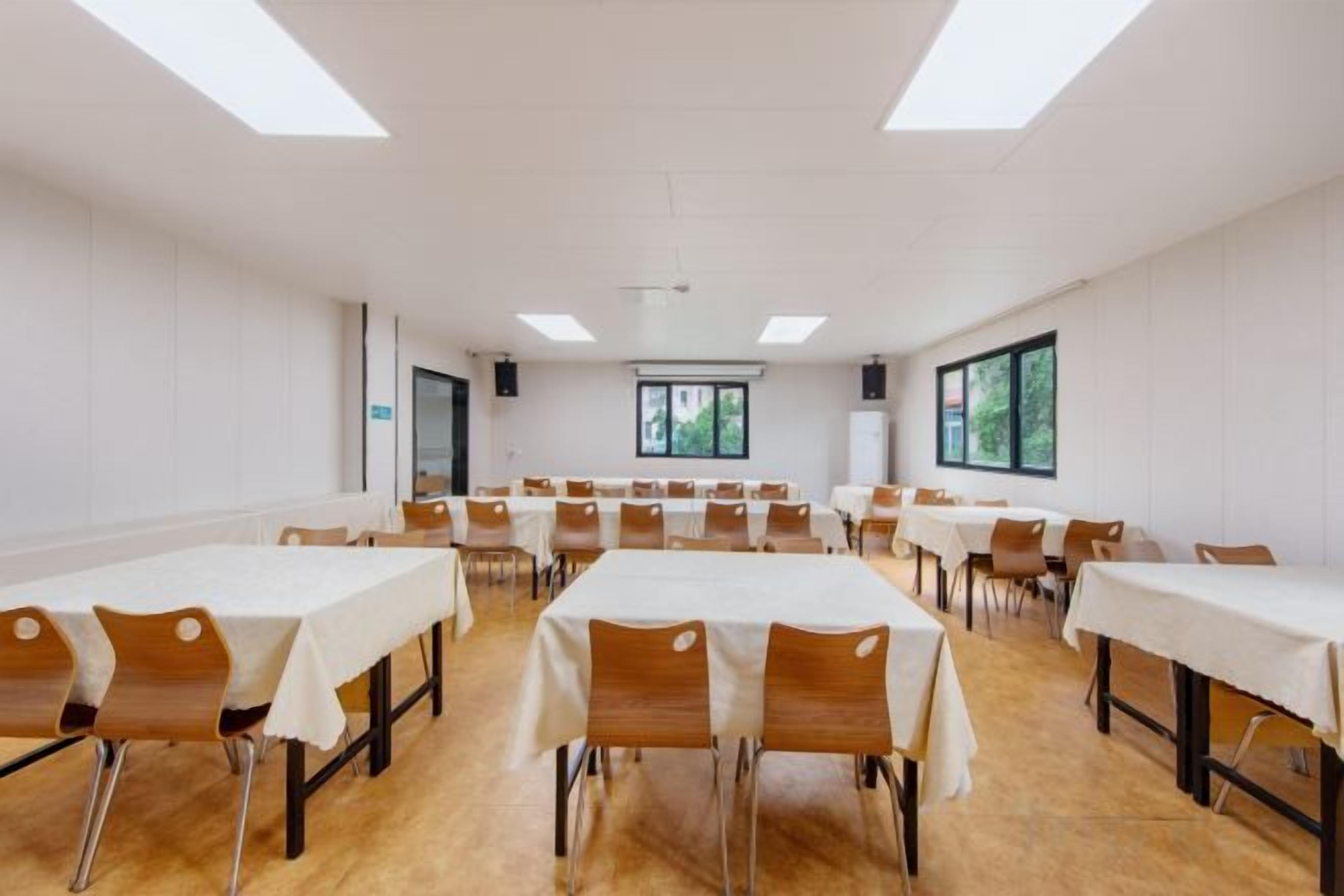 A conference room with multiple tables and chairs, large windows, and a white ceiling.