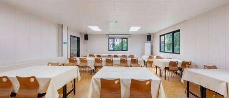A conference room with multiple tables and chairs, large windows, and a white ceiling.