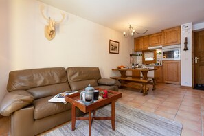 A living room with a brown leather sofa, a wooden coffee table with a tray, and a kitchen area with wooden cabinets and a stove.
