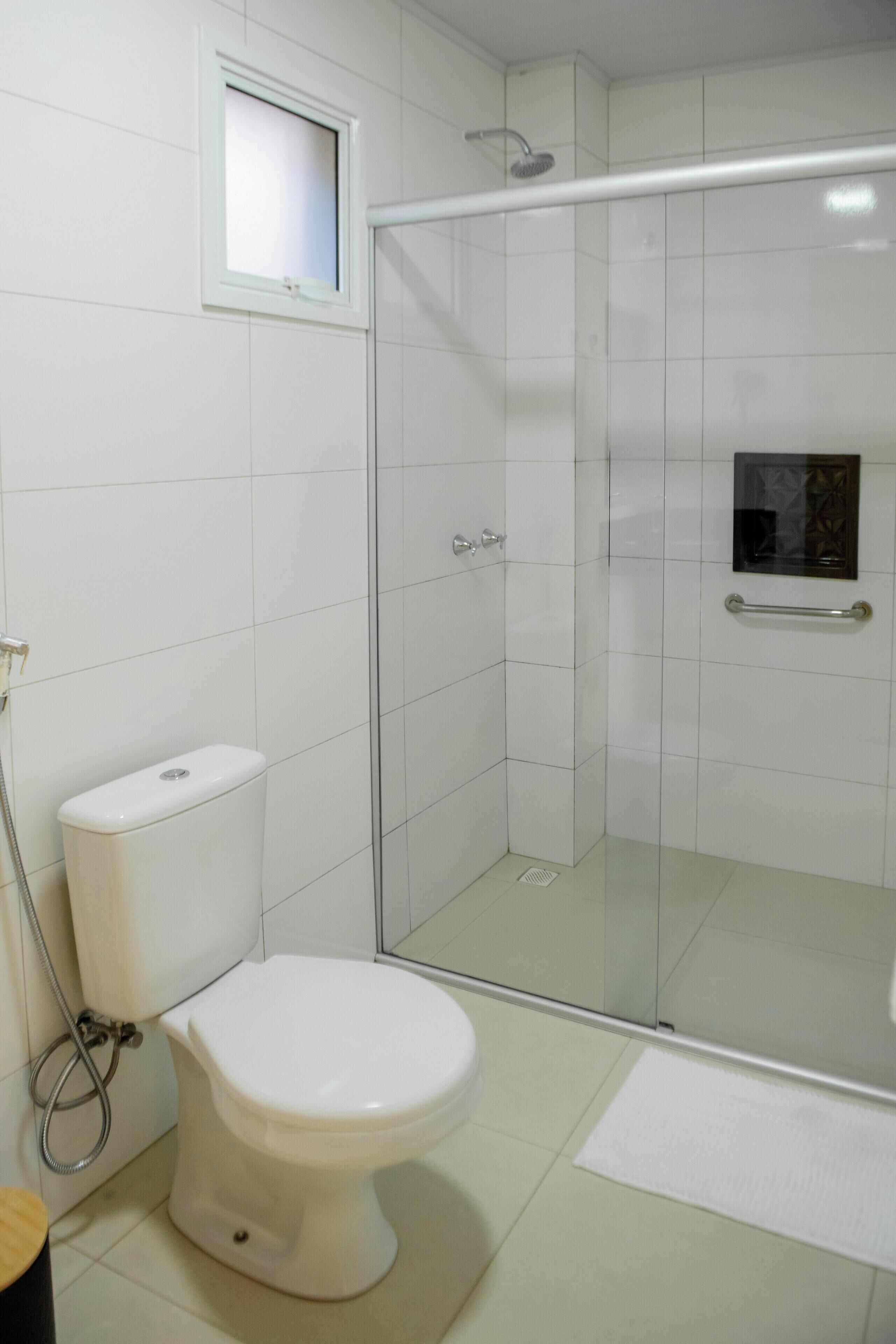 A bathroom with a toilet, a glass shower enclosure, and a small window.