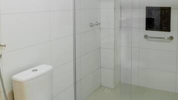 A bathroom with a toilet, a glass shower enclosure, and a small window.