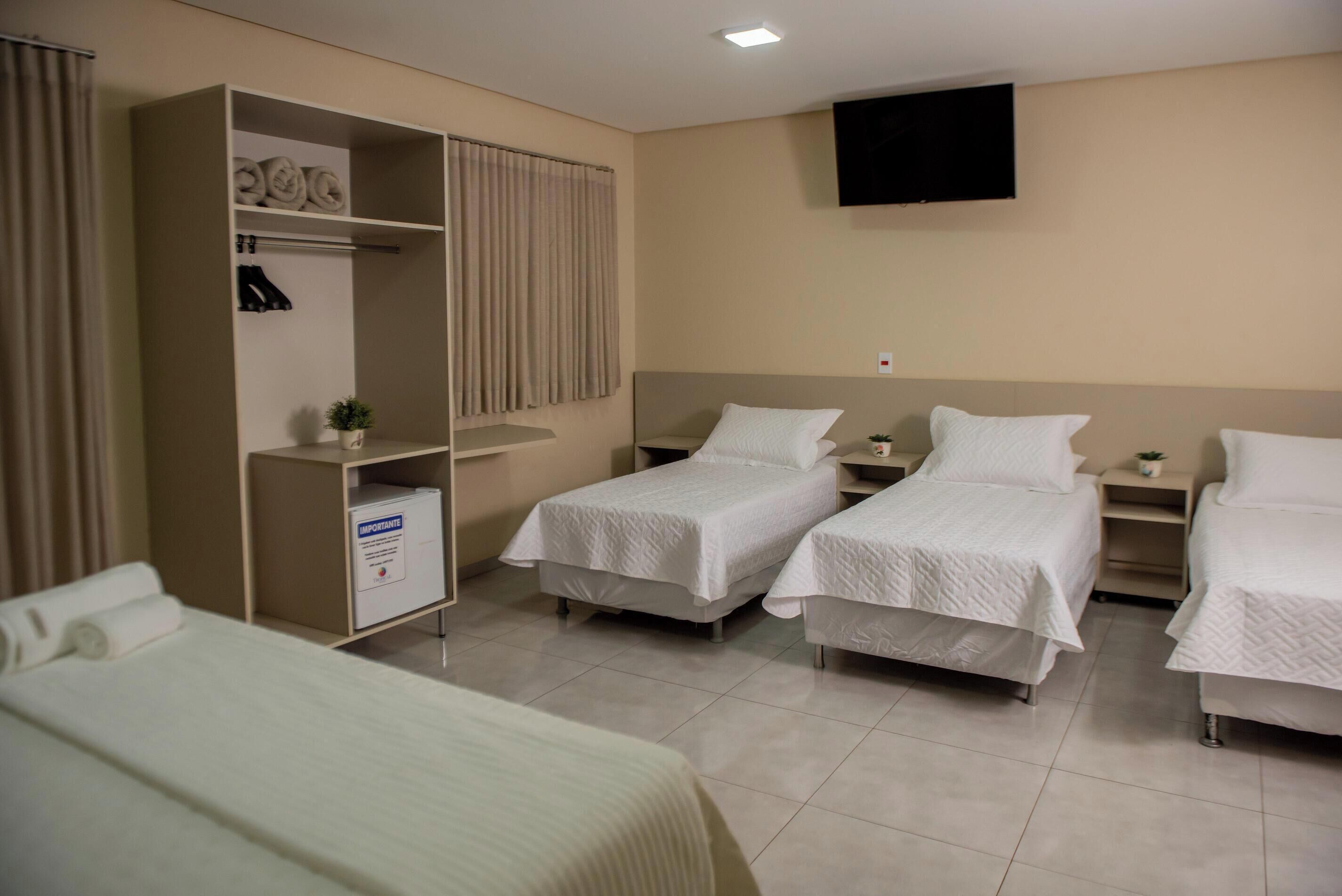 A hotel room with two single beds, a wardrobe, a television, and a small plant.