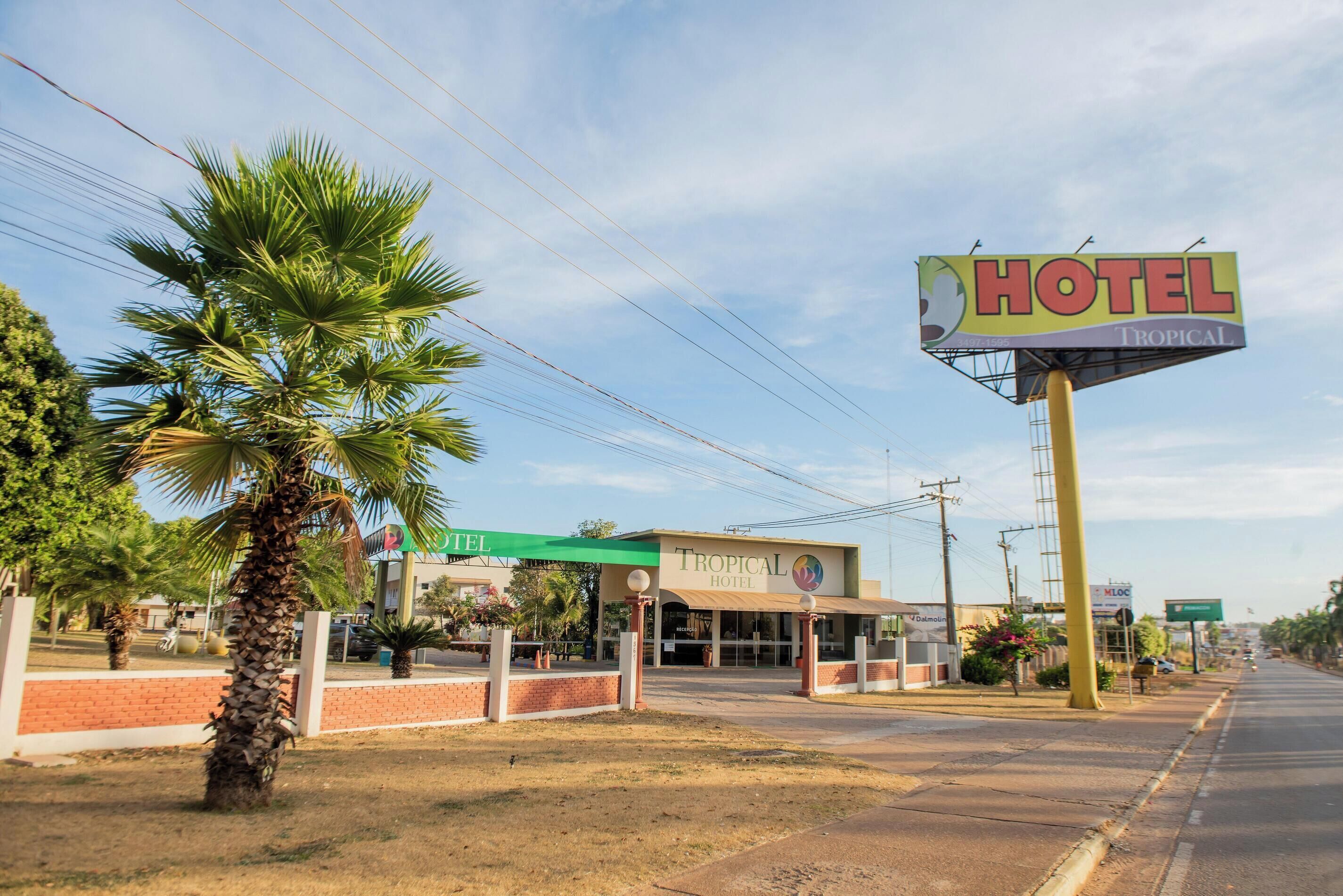 A hotel with a prominent sign, palm trees, and a clear sky.
