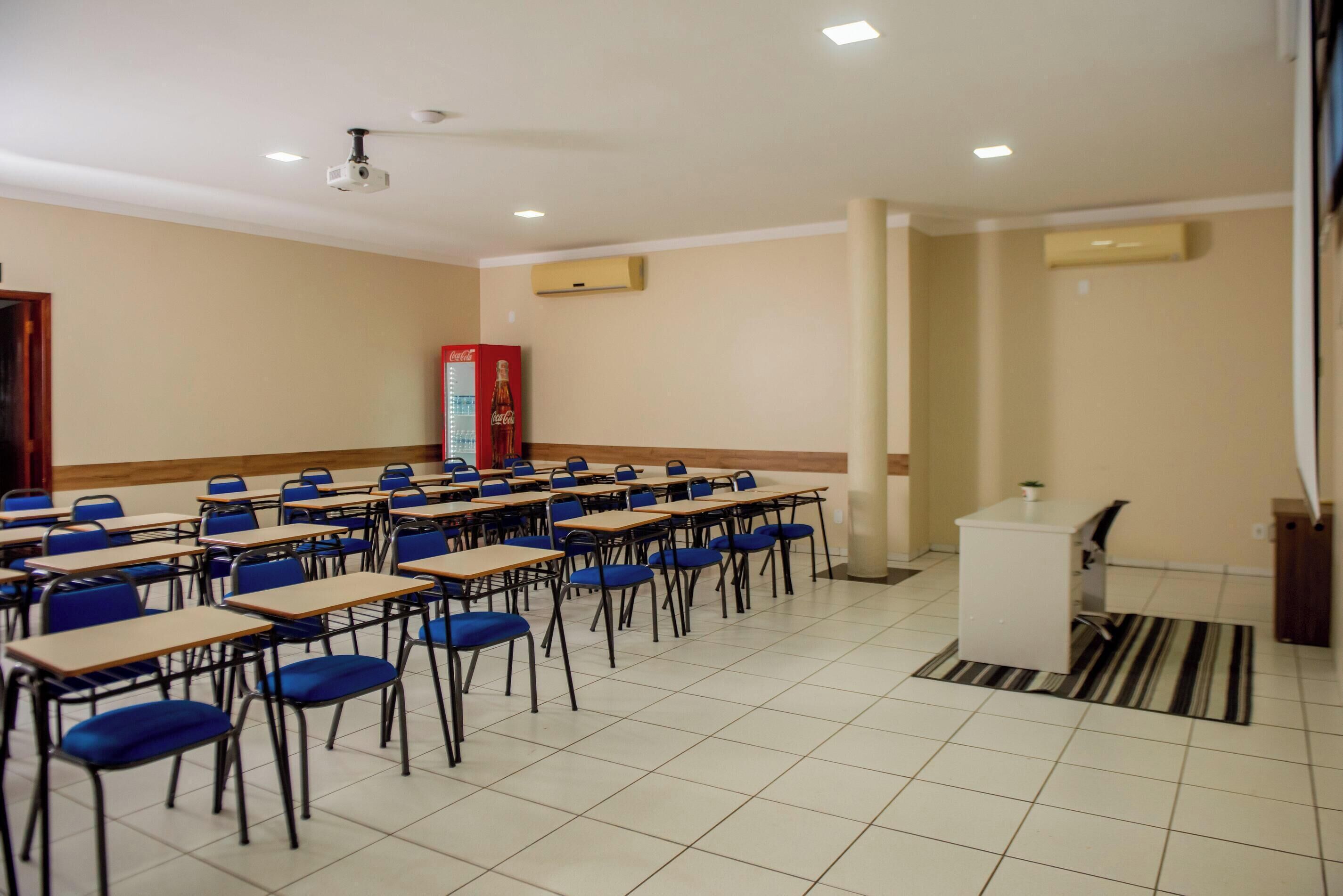 A classroom with rows of desks and chairs, a projector, and an air conditioning unit.