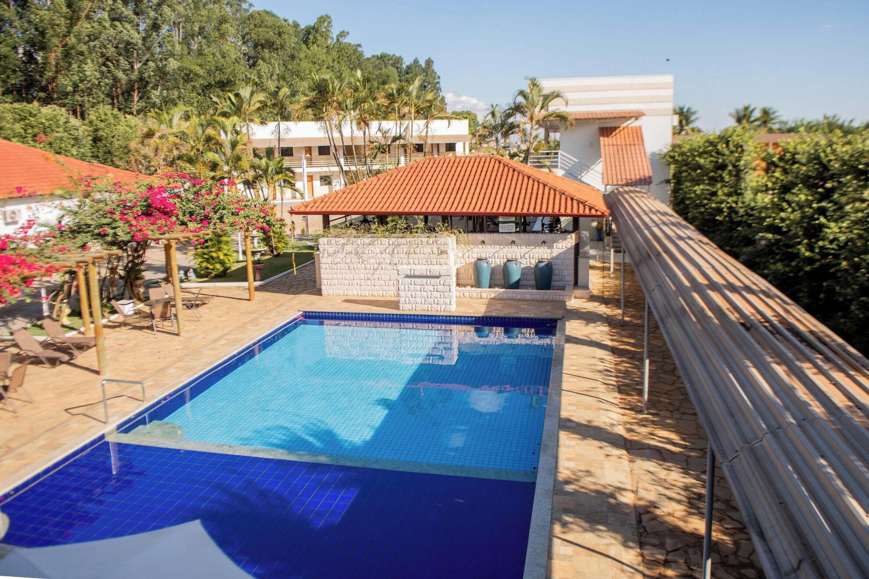 Una piscina con solárium de baldosas, rodeada por una valla de madera y un edificio con tejado rojo.
