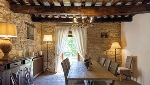 Une salle à manger rustique avec une table en bois, des chaises en osier, des murs en pierre et un lustre.