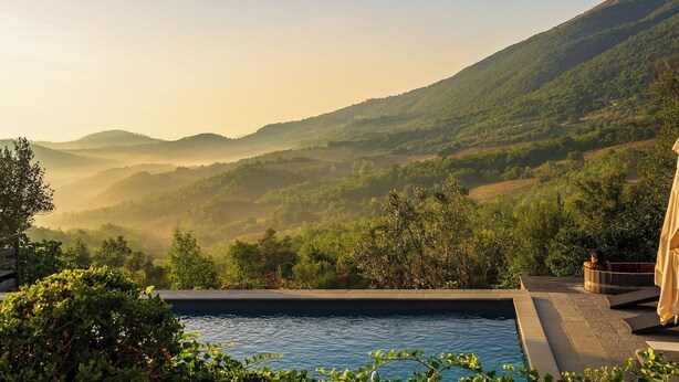 Une piscine offrant une vue sur des collines verdoyantes et un ciel dégagé.