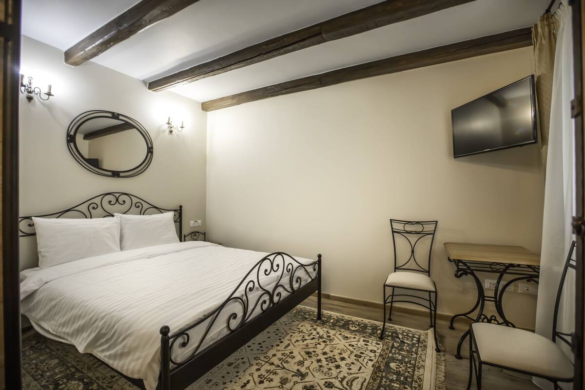 Ein Schlafzimmer mit einem Bett, einem Sessel, einem kleinen Tisch, einem Spiegel und einem an der Wand befestigten Fernseher.