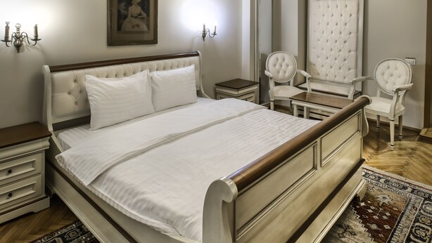 A bedroom with a large bed, a chandelier, a mirror, and two chairs. - Casa Gotica Residence (Brasov)
