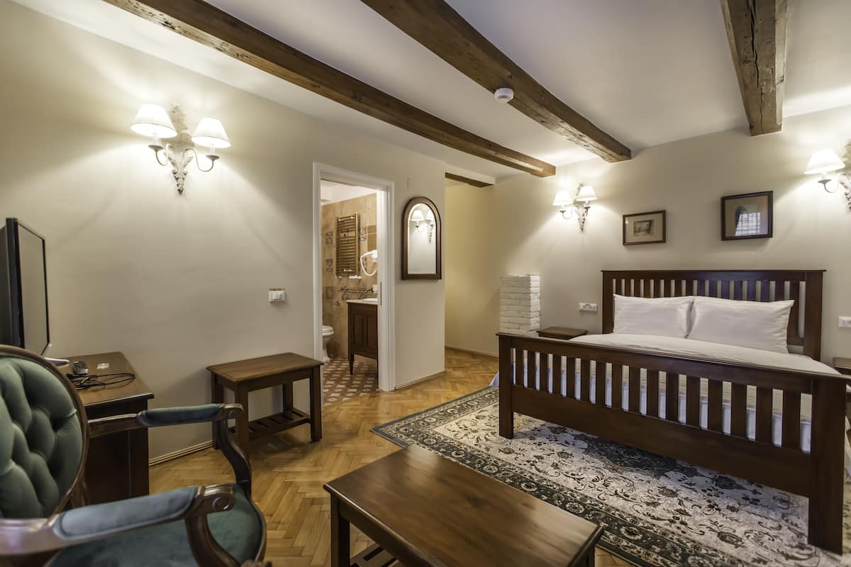 Ein Schlafzimmer mit einem hölzernen Bett, einem Schreibtisch, einem Stuhl und einem Spiegel. Ein Badezimmer ist durch eine geöffnete Tür sichtbar.