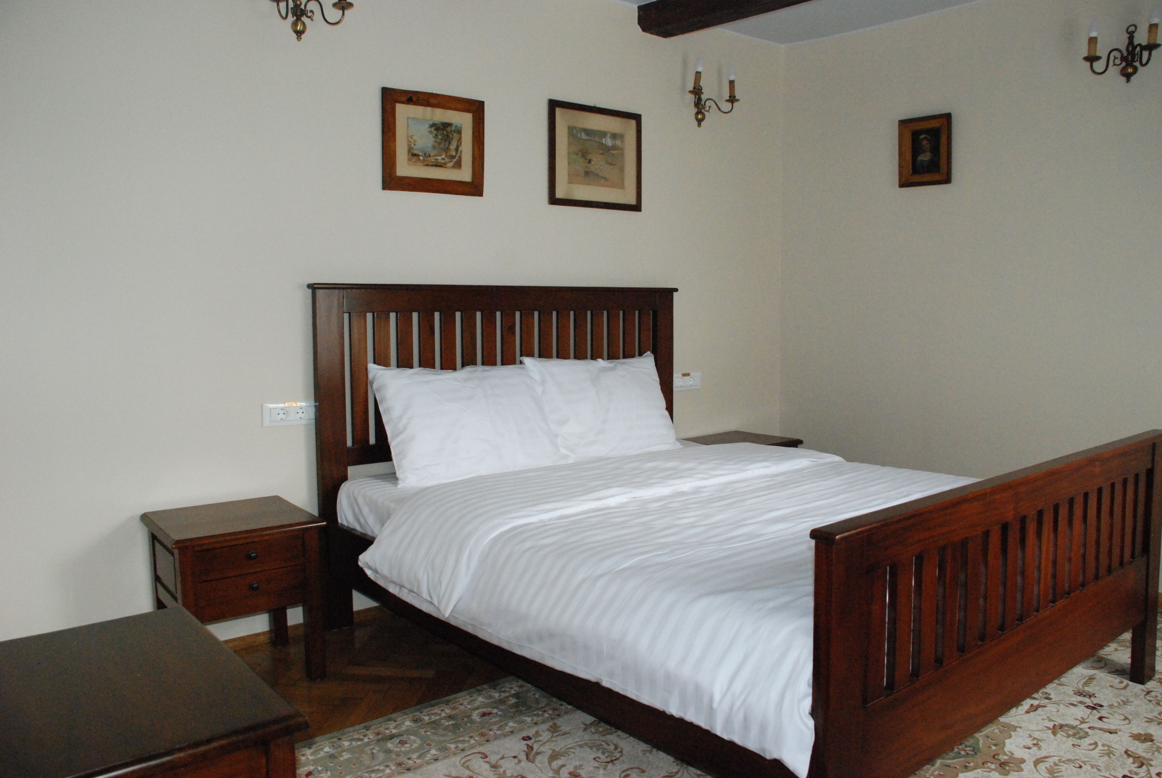 Une chambre à coucher avec un lit en bois, une table de chevet et une petite table. Trois tableaux encadrés sont accrochés au mur.