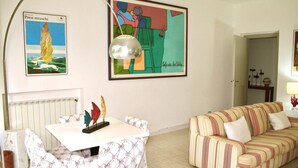 Uma sala de estar com um sofá riscado, uma mesa com toalha branca e duas obras de arte emolduradas na parede.