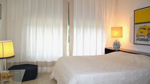 Quarto de hotel com uma cama, mesa de cabeceira com luminária, um vaso e um quadro na parede.