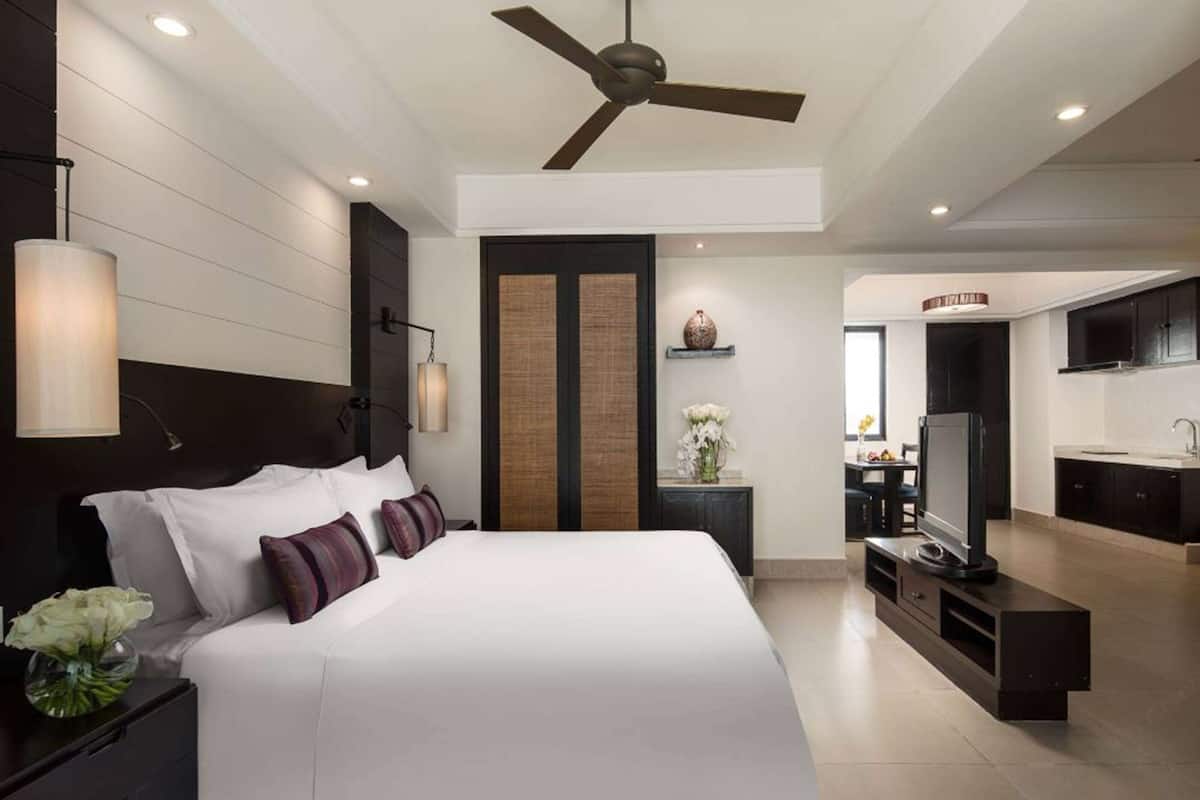 Una habitación de hotel moderna con una cama grande, ventilador de techo, televisor y kitchenette.