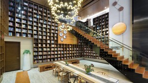 Eine moderne Bibliothek mit mehreren Etagen, Holzbögen, einer zentralen Treppe und einem langen Tisch mit Stühlen.