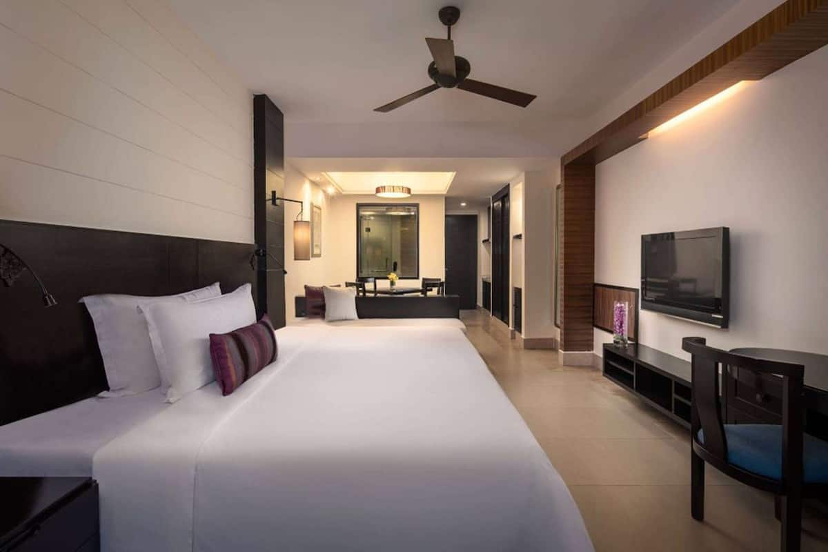 Habitación de hotel moderna con una cama grande, televisión, ventilador de techo y un pequeño rincón de descanso.