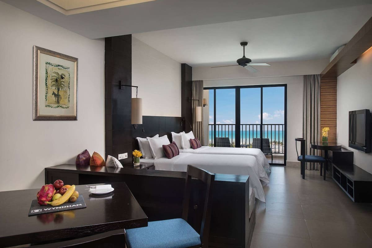Una habitación de hotel con cama, escritorio con fruta, televisor y balcón con vistas.