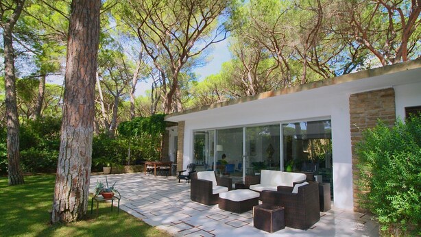 Een moderne buitenpatio met rieten meubilair, een afsluitbare eethoek met glas en een stenen muur.