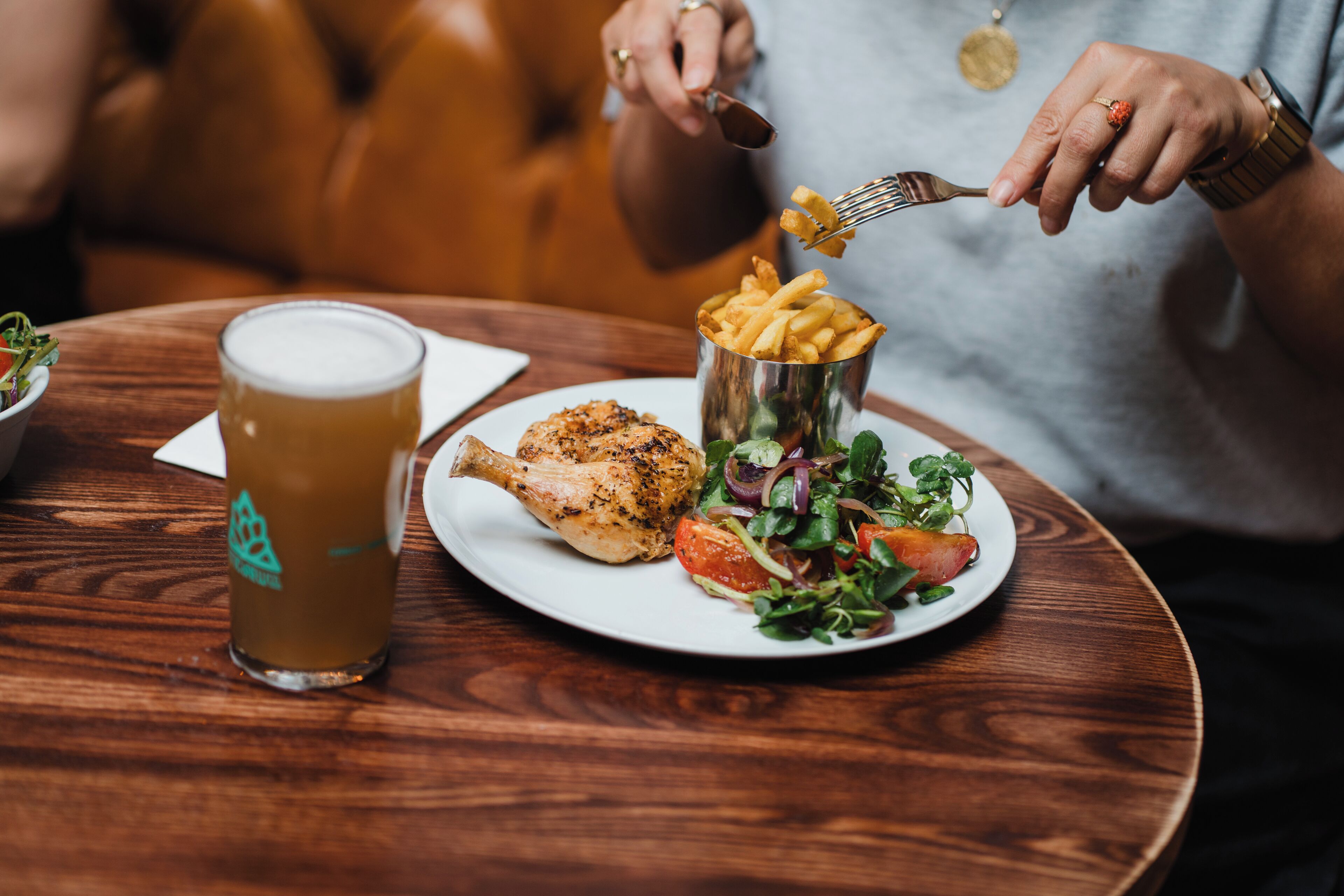 A meal with a grilled chicken leg, a glass of beer, and a side of fries and salad on a wooden table.