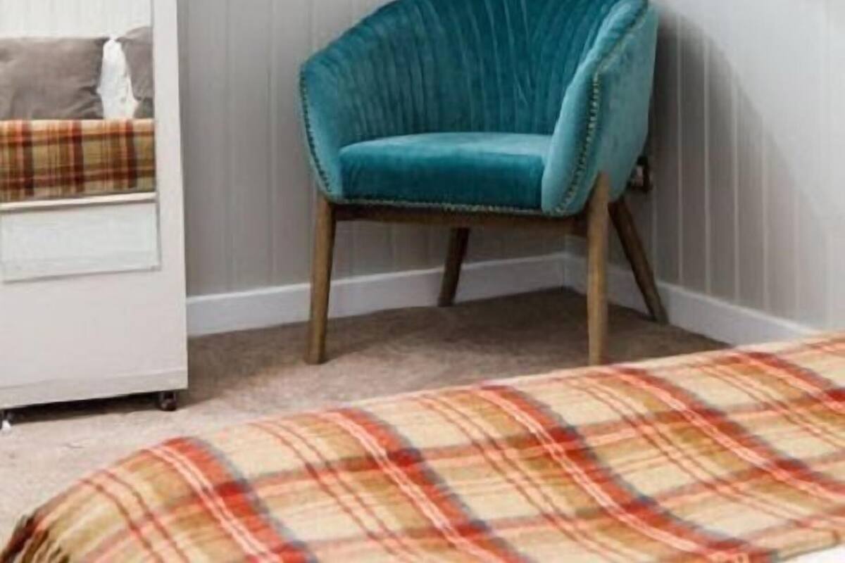 A room with a teal chair, a plaid bedspread, and a white wardrobe.