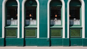 A building with four arched windows, each with a white frame and green shutters.
