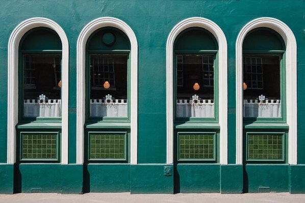 A building with four arched windows, each with a white frame and green shutters. - The Royal Sutton (Sutton Coldfield)