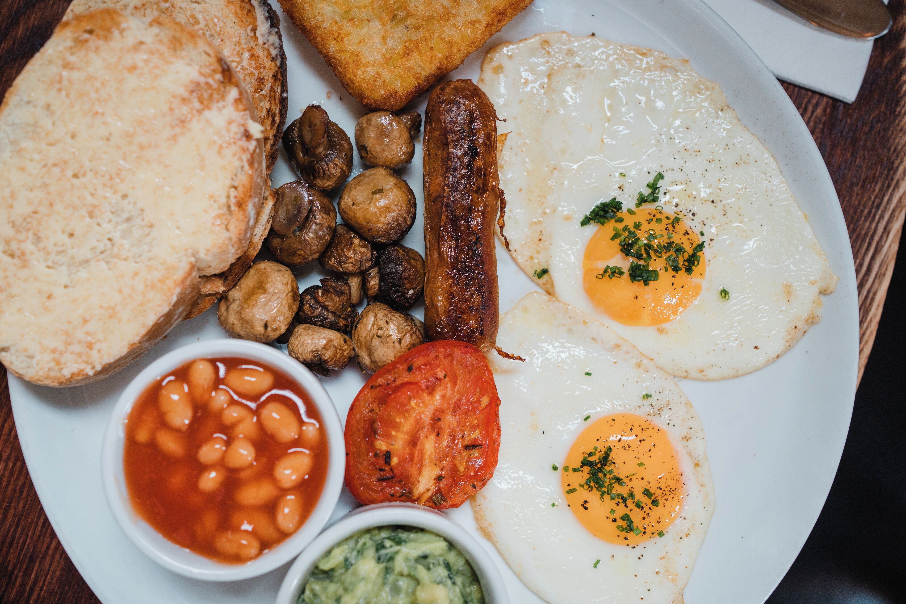 A plate with toast, sausages, mushrooms, eggs, beans, tomato, and sauce.
