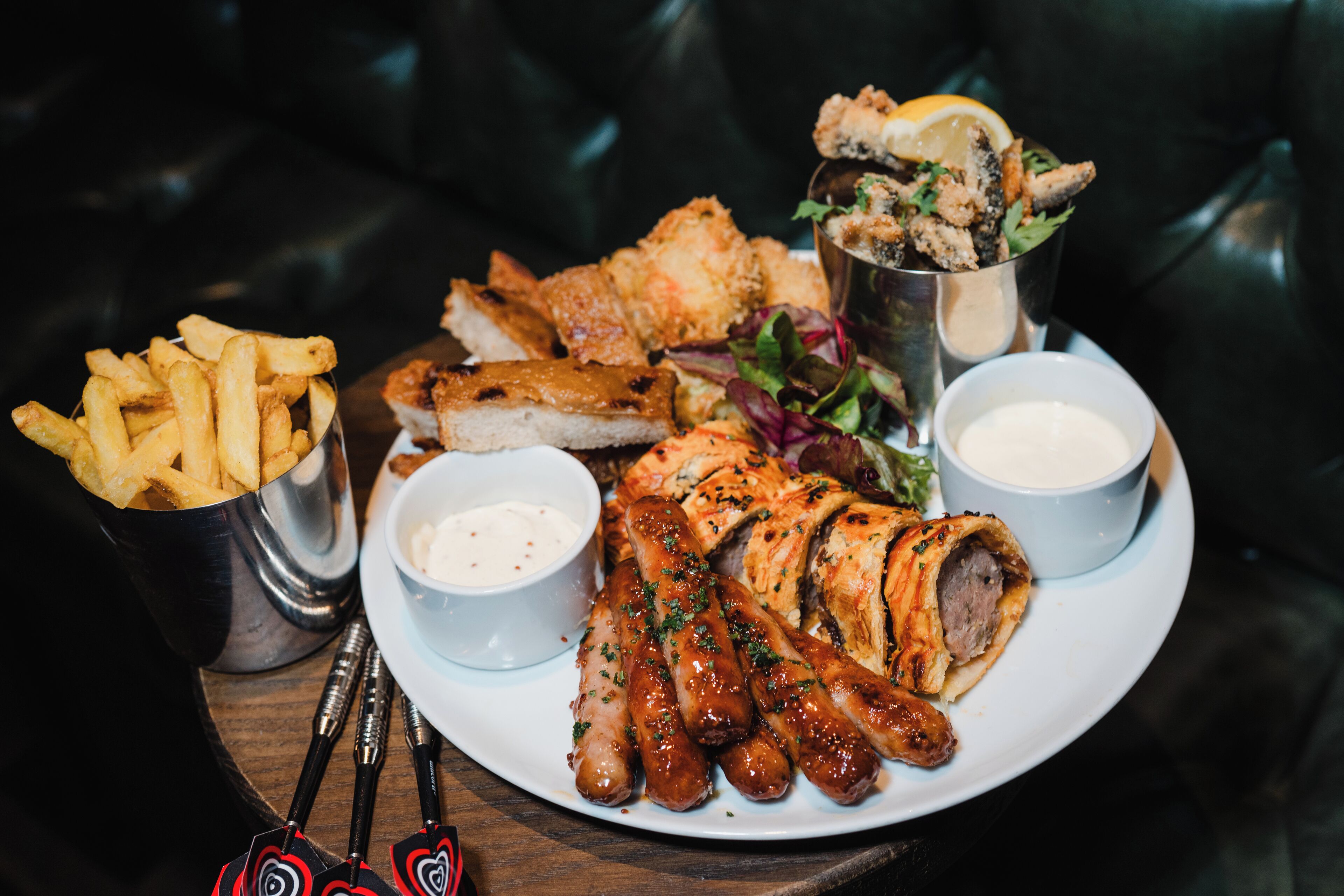 A plate of food including sausages, fish, chips, and salad with dipping sauces.