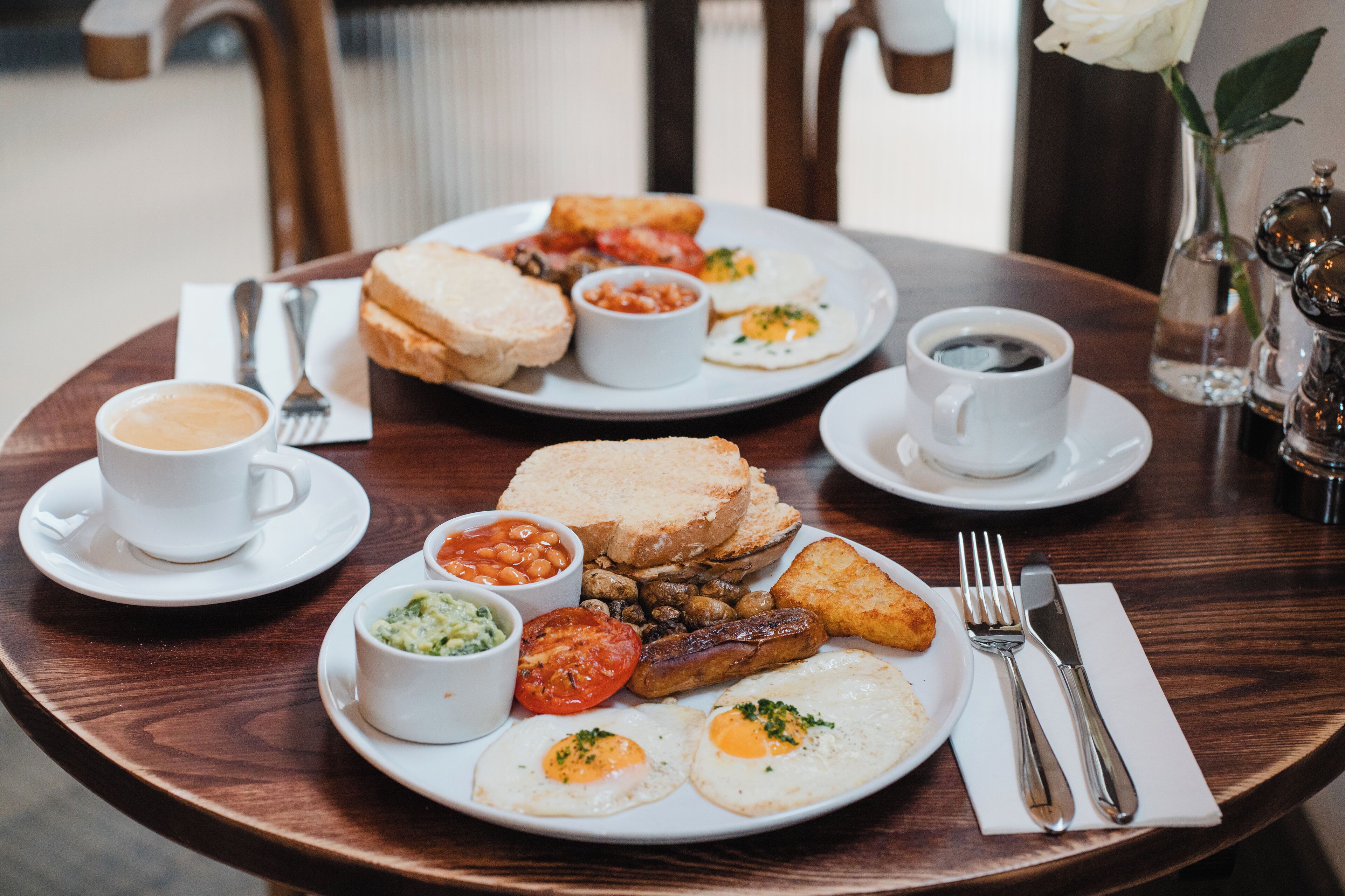 Un desayuno con platos de huevos, salchichas, tostadas, frijoles y una taza de café.
