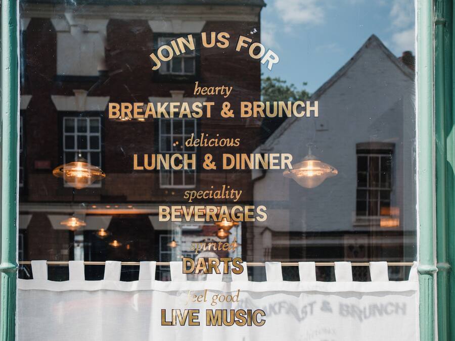Ein Fenster mit einem Schild, das Frühstück, Mittagessen, Abendessen, spezielle Getränke, Darts und Live-Musik bewirbt.