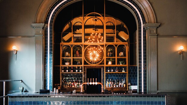 A bar area with a large arched window, shelves with bottles, and a central chandelier.
