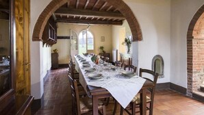 Une salle à manger avec une longue table dressée pour le repas, des chaises en bois et un plafond voûté en briques.