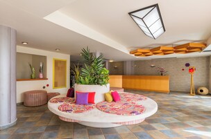 Un hall con una zona de estar circular, un mostrador de recepción y una planta grande.